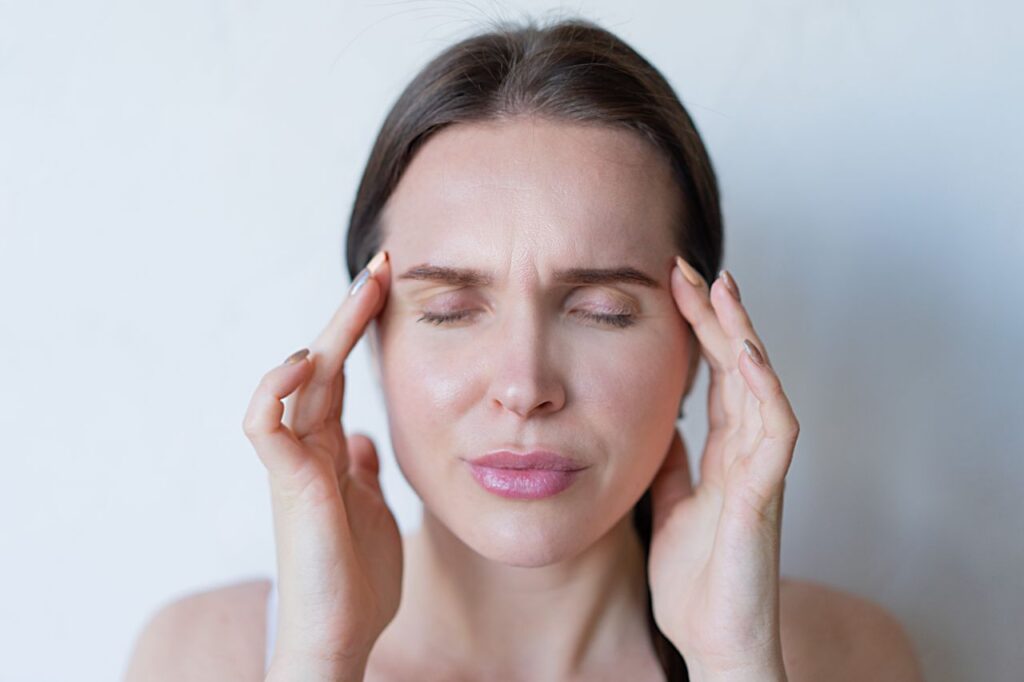 Close-up of a woman with closed eyes holding her temples, showing signs of a migraine or headache.